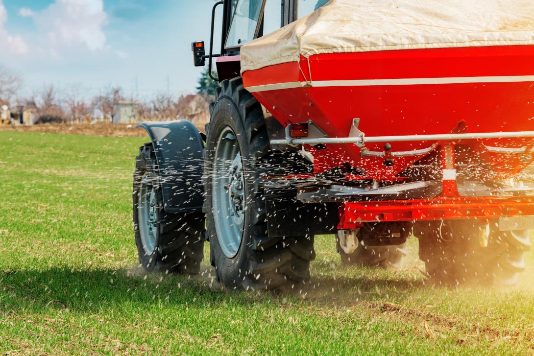 Ein Traktor mit Düngerstreuer fährt über ein Feld