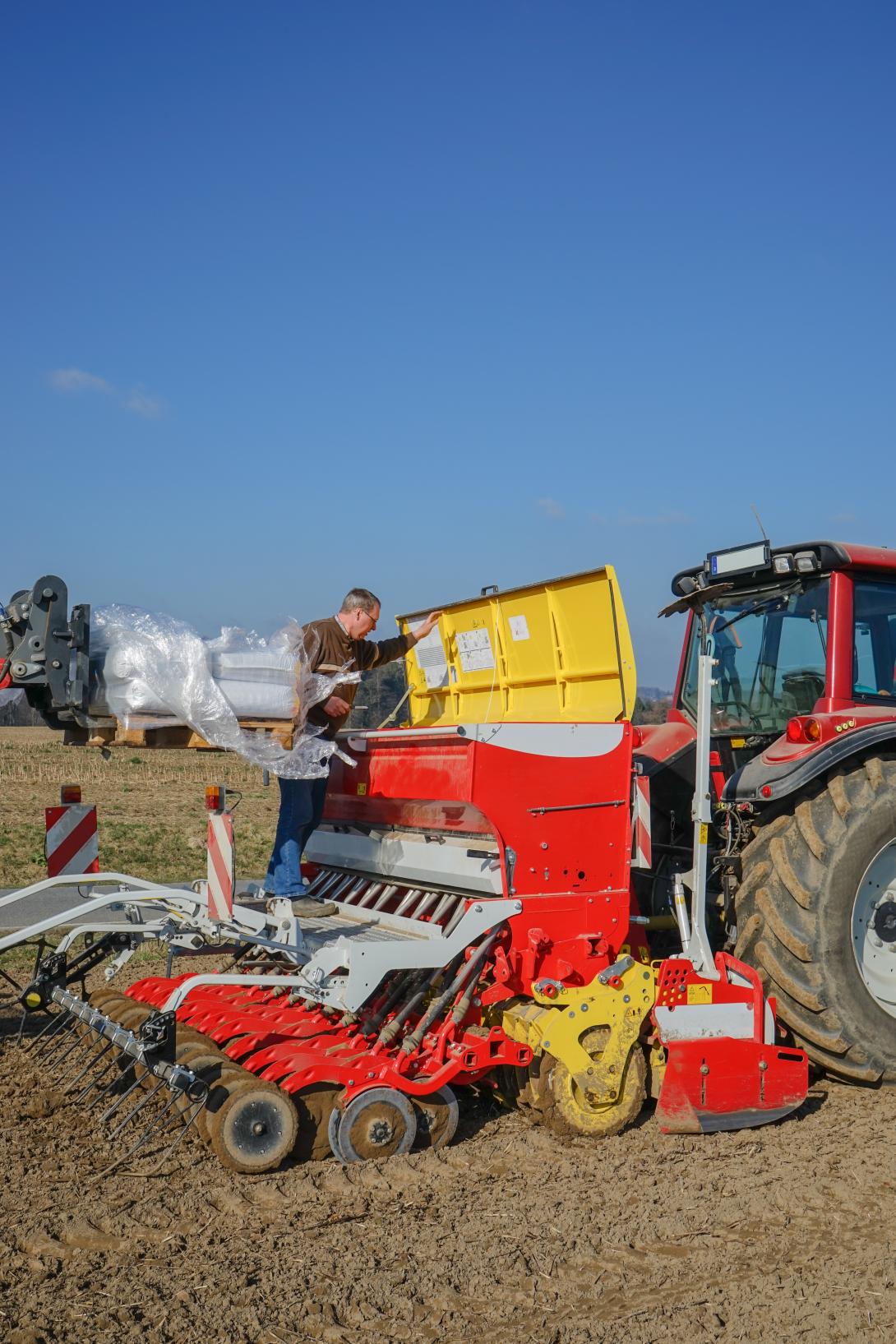 Landwirt beim Befüllen einer Sämaschine auf einem Feld.