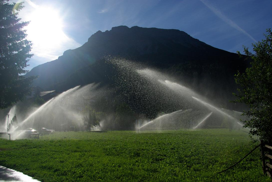 Wassersprenger, die eine Wiese bewässern, im Hintergrund ein Berg