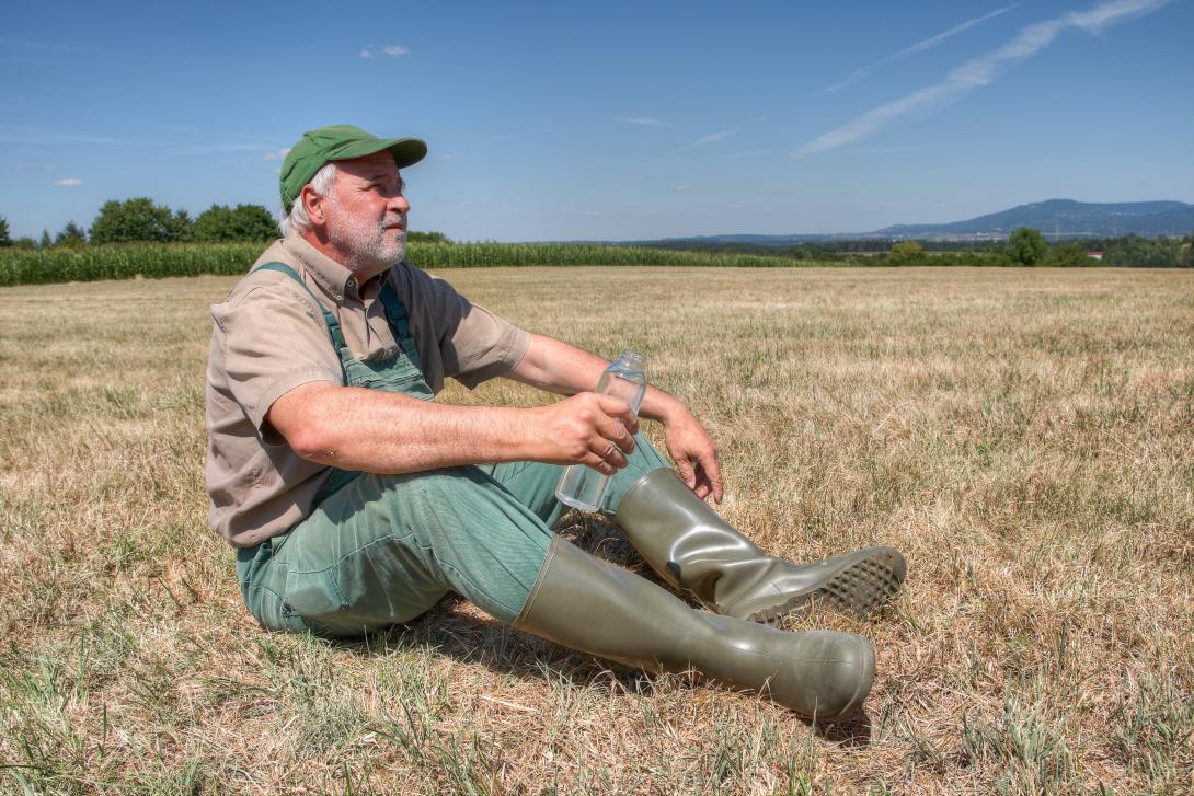 Landwirt sitzt auf einer vertrockneten Wiese